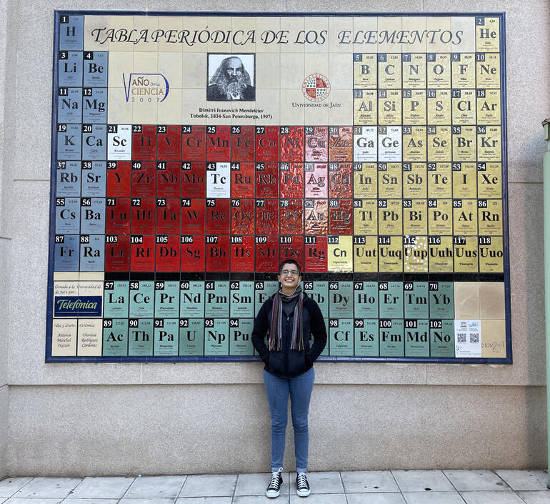 Mujer posando frente a una tabla periódica