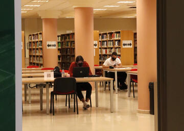 Imagen de una sala de la biblioteca con dos personas estudiando con mascarilla